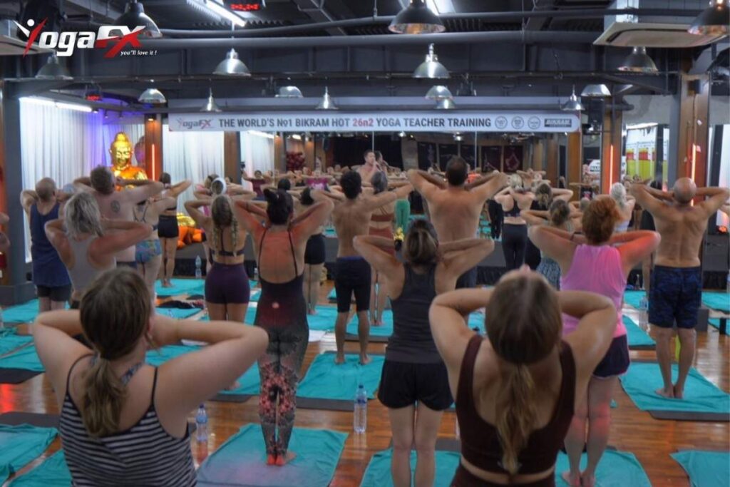 Trainee practicing live Bikram dialogue delivery in a heated studio, the in-person component online bikram yoga teacher training cannot fully replace.