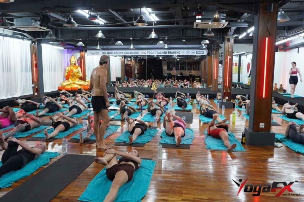 An instructor supporting a beginner modifying postures safely during a Bikram class