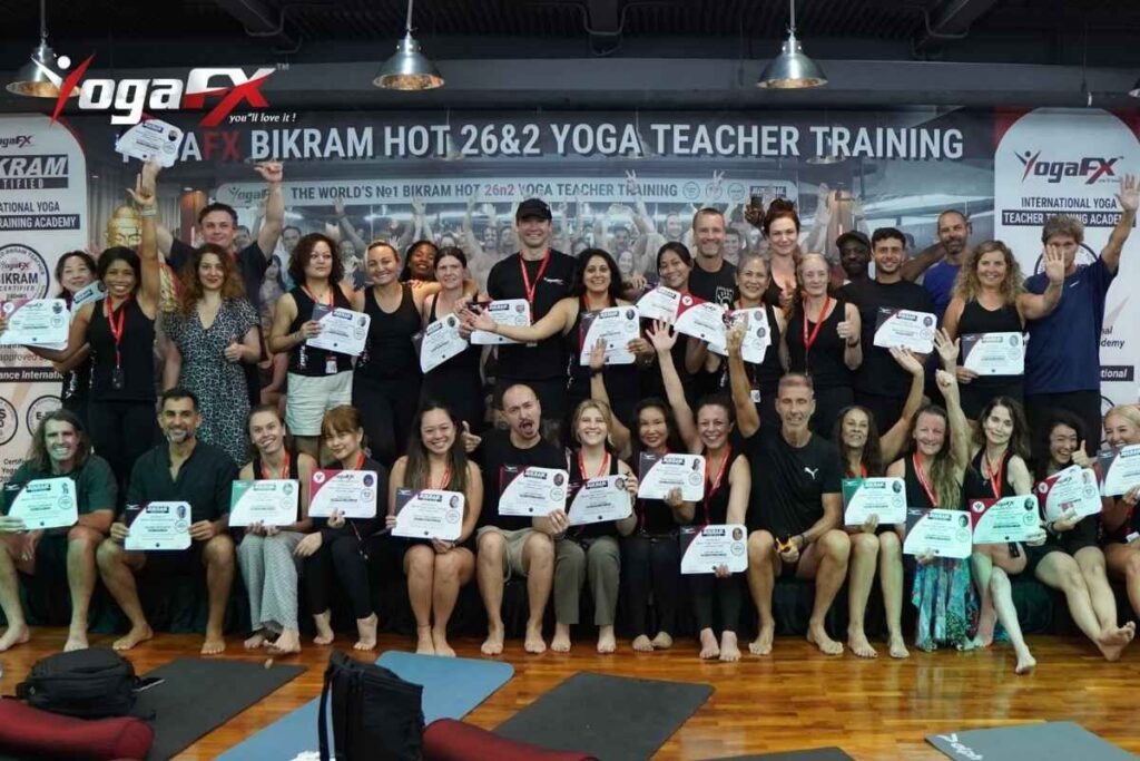 A dual-certified YogaFX Bali hot yoga instructor delivering the scripted 26&2 dialogue to students mid-posture in the heated Canggu studio room