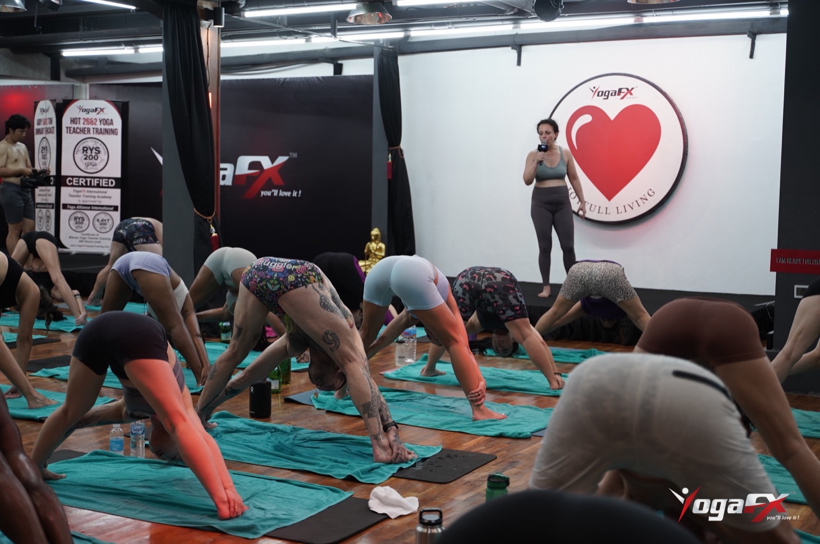 A hot yoga class folding forward together, with a male student in the foreground working through the posture
