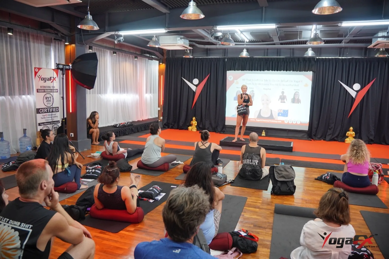 Wide view of the YogaFX Bali studio with students seated on mats as a teacher presents at the front, a calm setting for a sauna after hot yoga plan